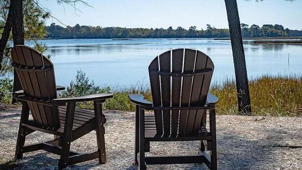 Kaksi Adirondack-tyylistä tuolia, jotka on asetettu vastakkain järven tai muun vesistön ääreen, ja taustalla näkyy puita.