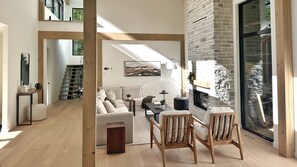 Ein modernes Wohnzimmer mit Kamin, Holzbalken, einer Treppe und einem großen Fenster.