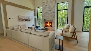 Ein Wohnzimmer mit Kamin, einer Couch, einem Sessel und großen Fenstern.