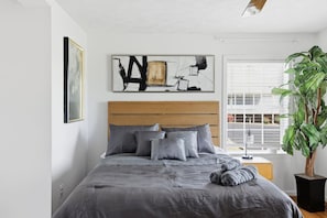 Una camera da letto con un letto, un comodino, una pianta in vaso e opere d'arte alle pareti.