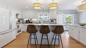 Una cocina moderna con armarios blancos, una isla central con taburetes e iluminación colgante.