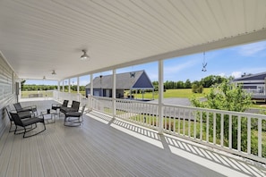 A covered outdoor deck with seating, a view of a house, and a fenced area. - Fairway Farmhouse | Stay & Play Disc Golf Course! (Quinton)