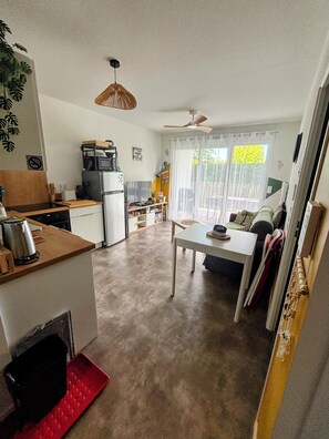 Eine kompakte Küche mit Kühlschrank, Mikrowelle und Herd, ein Essbereich mit Tisch und Stühlen sowie ein Deckenventilator.