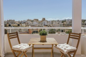 Ein Balkon mit zwei Holzstühlen, einem Tisch, einem Blumentopf und Blick auf die Stadt.