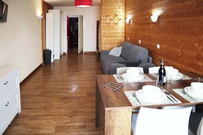 Ein Zimmer mit Holzwandverkleidung, einem Esstisch für vier Personen, einer Couch und einem weißen Schminktisch.