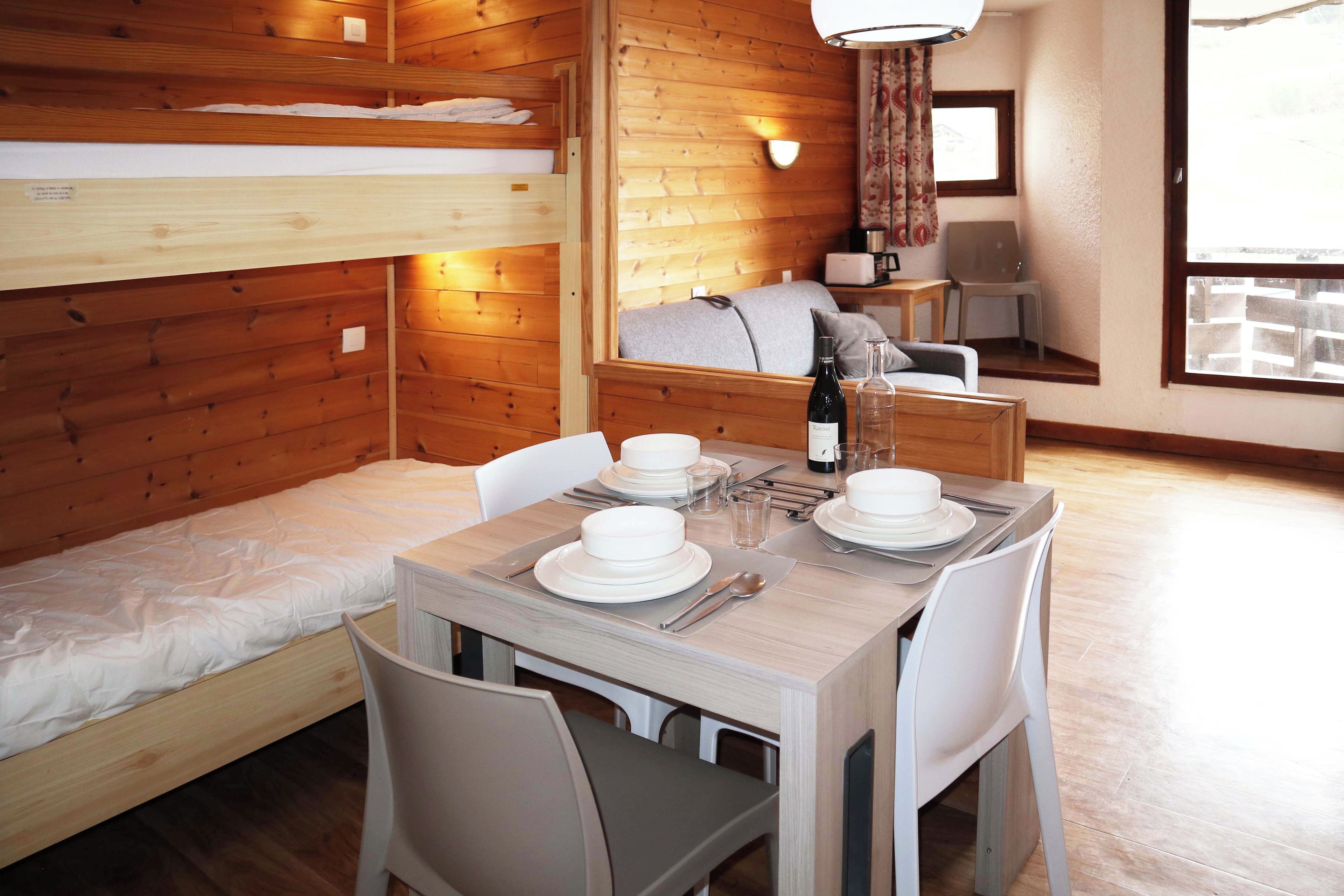 A room with bunk beds, a dining table set for two, and a window with a view.