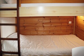 Un lit superposé avec une tête de lit en bois et un lit inférieur doté d’un matelas blanc.