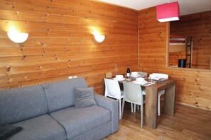 Ein Zimmer mit Holzwänden, einem grauen Sofa, weißen Stühlen, einem Holztisch und zwei Wandleuchten.