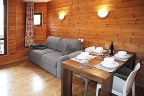 Ein Zimmer mit Holzwandverkleidung, einer Couch, einem Esstisch für vier Personen und zwei Wandleuchten.