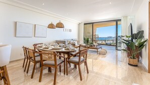 Zona pranzo con tavolo rotondo, sedie e vista sulla città attraverso ampie finestre.