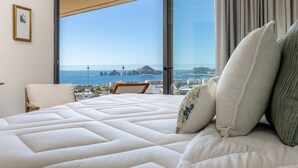 Una camera da letto con un letto grande, una sedia, vista sul mare e una finestra con tende.