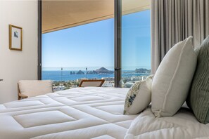 Ein Schlafzimmer mit einem großen Bett, einem Sessel, Blick aufs Meer und einem Vorhangfenster.