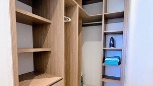 A walk-in closet with wooden shelving and drawers, a small shoe rack, and a folded towel on one of the shelves. - Penthouse | Ocean Views, Pools & Padel Court (Cabo San Lucas)