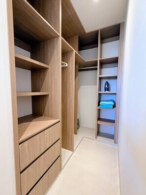 A walk-in closet with wooden shelving and drawers, a small shoe rack, and a folded towel on one of the shelves. - Penthouse | Ocean Views, Pools & Padel Court (Cabo San Lucas)