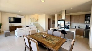 A modern open-plan living area with a dining table, sofa, and kitchen. - Penthouse | Ocean Views, Pools & Padel Court (Cabo San Lucas)