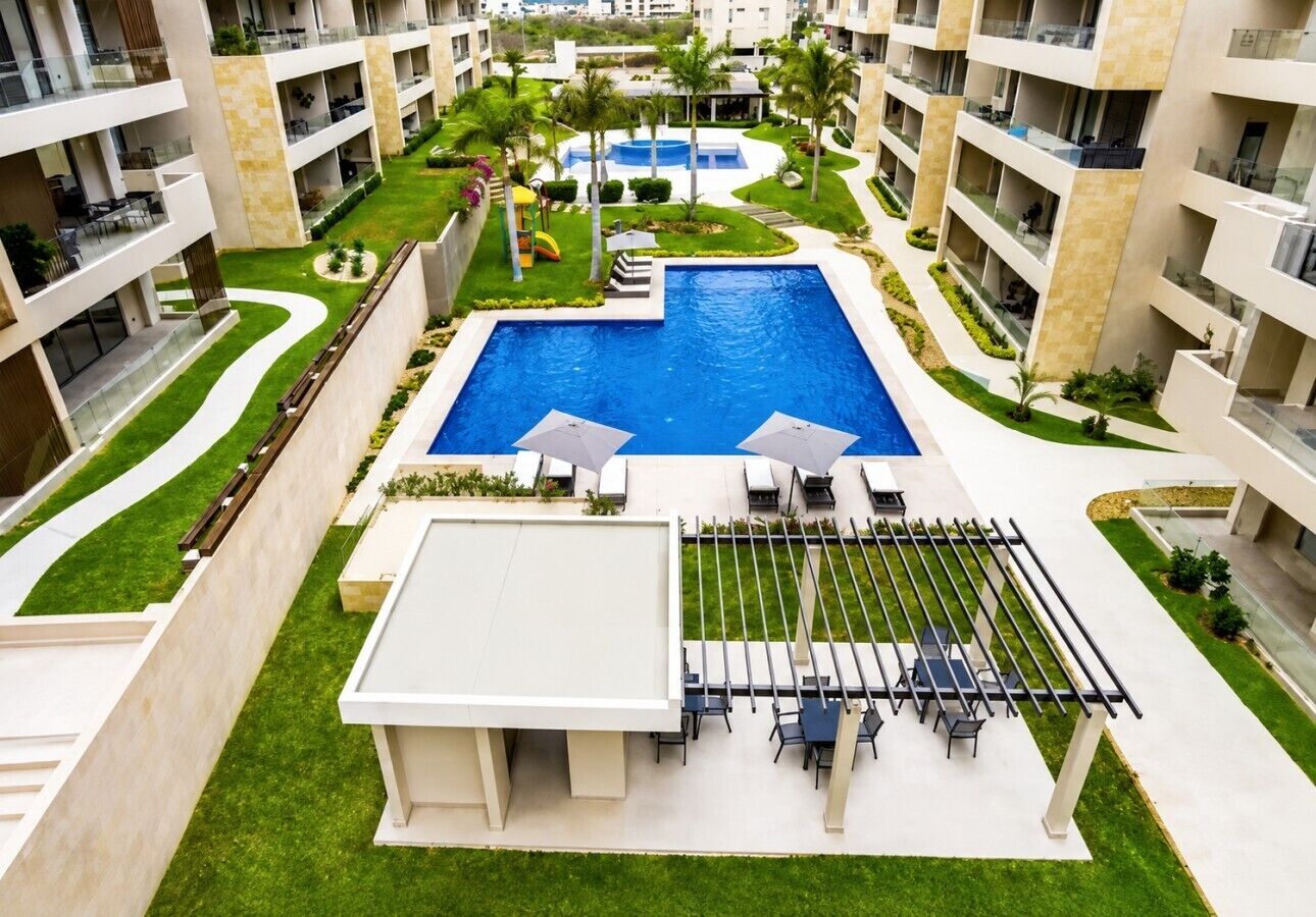 Un hotel moderno con piscina central, mobiliario exterior y exuberante jardinería.