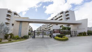 A modern apartment complex entrance with a gated driveway, a central archway, and a sign reading 'VISTA VELA III'. - Penthouse | Ocean Views, Pools & Padel Court (Cabo San Lucas)