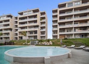 Ein modernes Hotel mit Swimmingpool, mehreren Balkonen und einem angelegten Garten mit Liegestühlen.