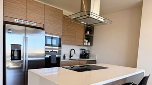 A modern kitchen with stainless steel appliances, a central island, and black bar stools. - Penthouse | Ocean Views, Pools & Padel Court (Cabo San Lucas)