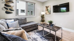 A modern living room with a grey sofa, a coffee table, and a flat-screen TV mounted on the wall. - Modern Townhome Rooftop Garage Stockyards Downtown (Fort Worth)