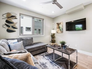 A modern living room with a grey sofa, a coffee table, and a flat-screen TV mounted on the wall. - Modern Townhome Rooftop Garage Stockyards Downtown (Fort Worth)