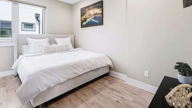 A bedroom with a bed, a window, a wall-mounted painting, and a small table with a plant. - Modern Townhome Rooftop Garage Stockyards Downtown (Fort Worth)