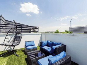 A rooftop patio with outdoor furniture, including a hanging chair and sofas with cushions.