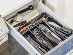 Eine Schublade mit verschiedenen Küchenutensilien, darunter Messer, Löffel und ein Sieb.