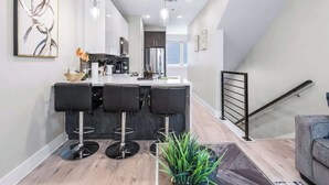 A modern kitchen with a central island, bar stools, and a staircase leading to an upper level. - Modern Townhome Rooftop Garage Stockyards Downtown (Fort Worth)