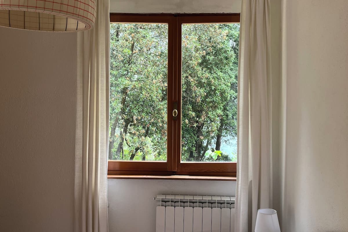 A bedroom with a bed, a radiator, a window with curtains, and a lamp on a bedside table.