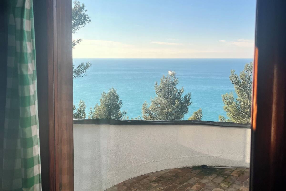 A balcony with a view of the sea, a checkered curtain, and a brick floor.