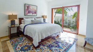 Quarto com cama, mesas de cabeceira, ventilador de teto, uma janela grande e um tapete colorido.