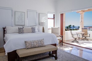 Ein Schlafzimmer mit einem großen Bett, einer Bank, einem Sessel und einem Tisch auf einem Balkon mit Blick.