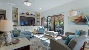 Sala de estar moderna com televisão, sofás, mesa de centro e área de jantar com vista.