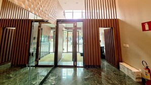 A hotel lobby with a geometric patterned wall, a glass door entrance, and a fire extinguisher on the right. - LK Savassi 6 (Belo Horizonte)