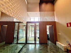 Un vestíbulo de hotel con un muro de diseño geométrico, una puerta de cristal de entrada y un extintor a la derecha.