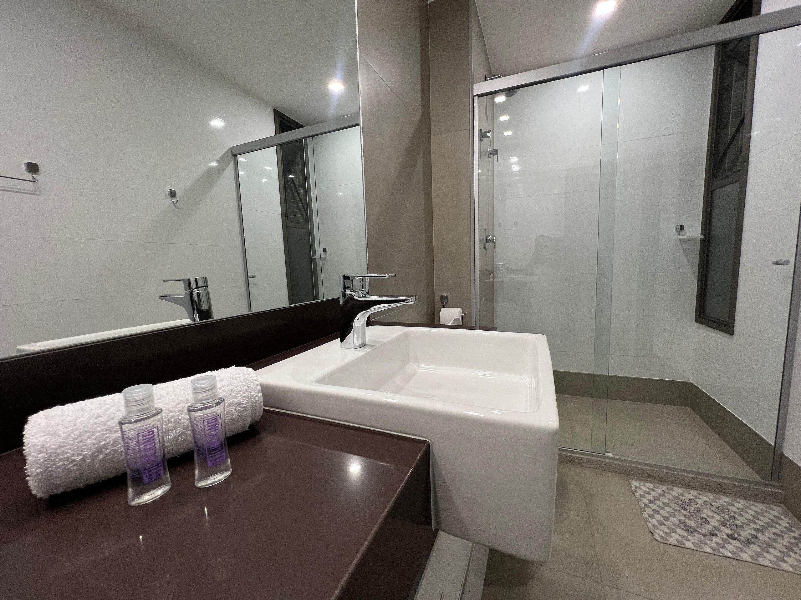 Un baño moderno con un espejo grande, un lavamanos blanco y una ducha con mampara de vidrio.