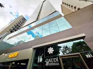 Un edificio moderno con fachada de vidrio, un llamativo letrero que dice 'GAUDI RESIDENCIA' y un letrero que dice 'BARBEARIA'.