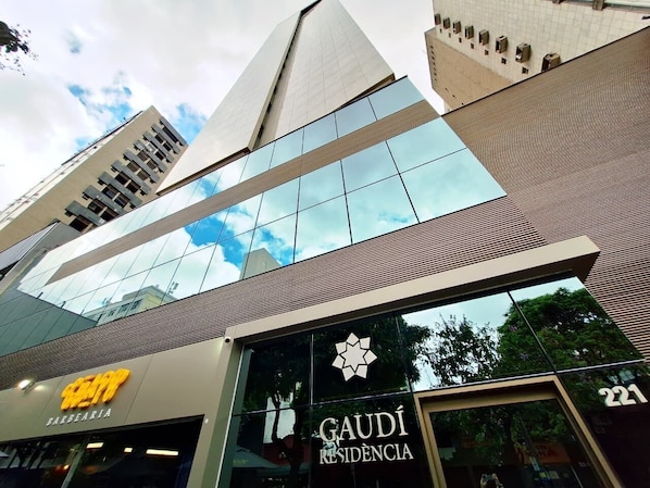 En modern byggnad med en fasad av glas, en framträdande skylt med texten ”GAUDI RESIDENCIA” och en skylt med texten ”BARBEARIA”.