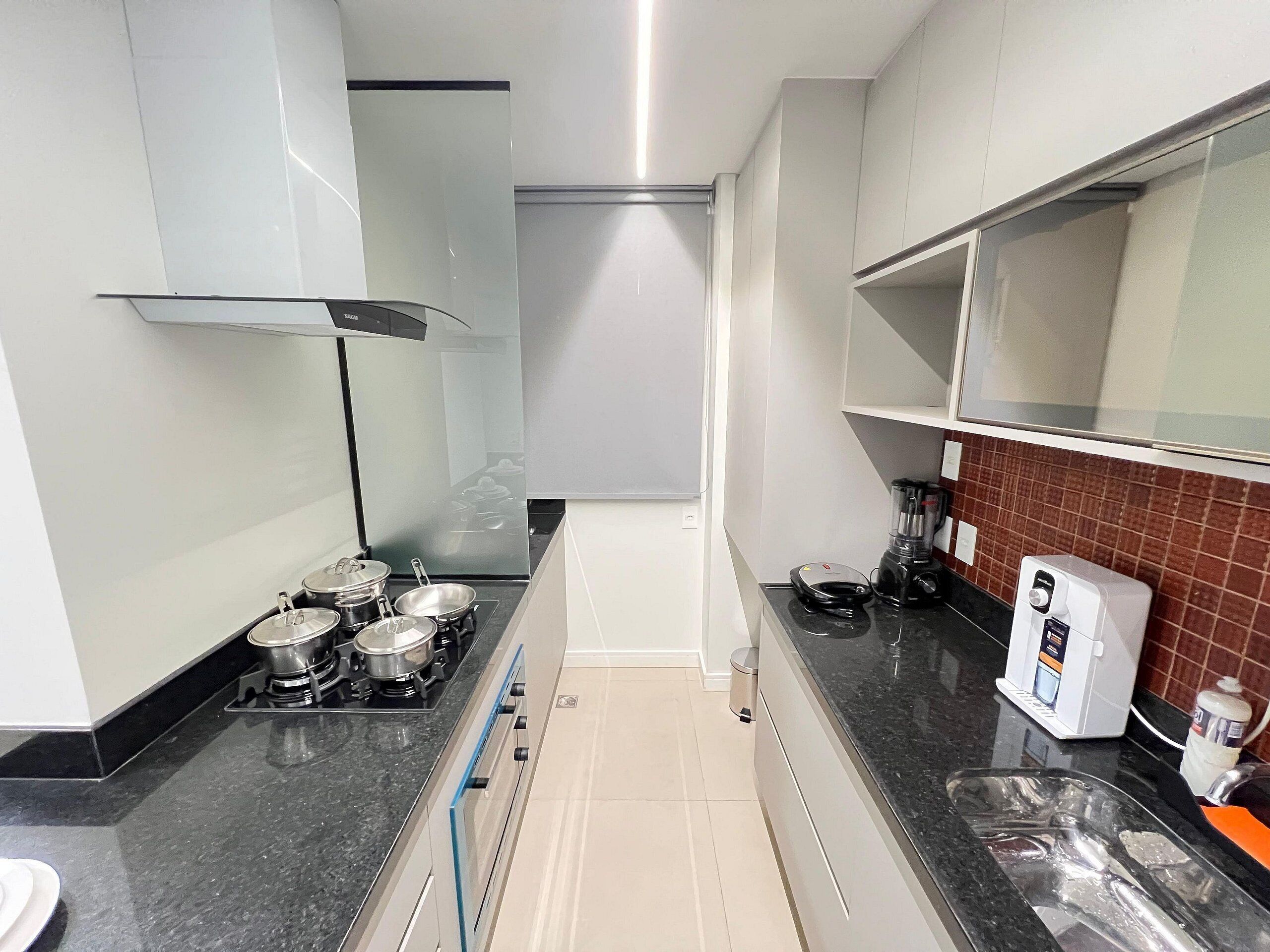 Una cocina con estufa, ollas, cafetera y un cubo de basura.