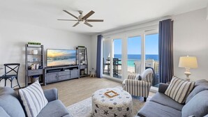 A living room with a large TV, a ceiling fan, a sofa set, a coffee table, and a view of the ocean. - Resort Condo w/ Gulf Views, 5 Pools & Hot Tubs (Panama City Beach)