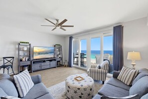 Ein Wohnzimmer mit großem Fernseher, Deckenventilator, Sofagarnitur, Couchtisch und Blick auf den Ozean.