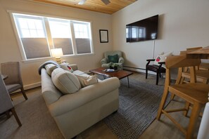 A living room with a sofa, coffee table, and a TV mounted on the wall. - 1 Br Suite in Downtown North Creek, with Views of Gore Mountain & Ski Bowl (North Creek)