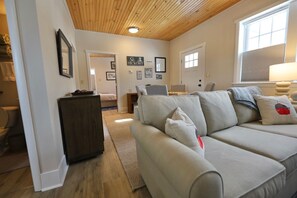 A living room with a wooden ceiling, a sofa, a coffee table, and a lamp. - 1 Br Suite in Downtown North Creek, with Views of Gore Mountain & Ski Bowl (North Creek)