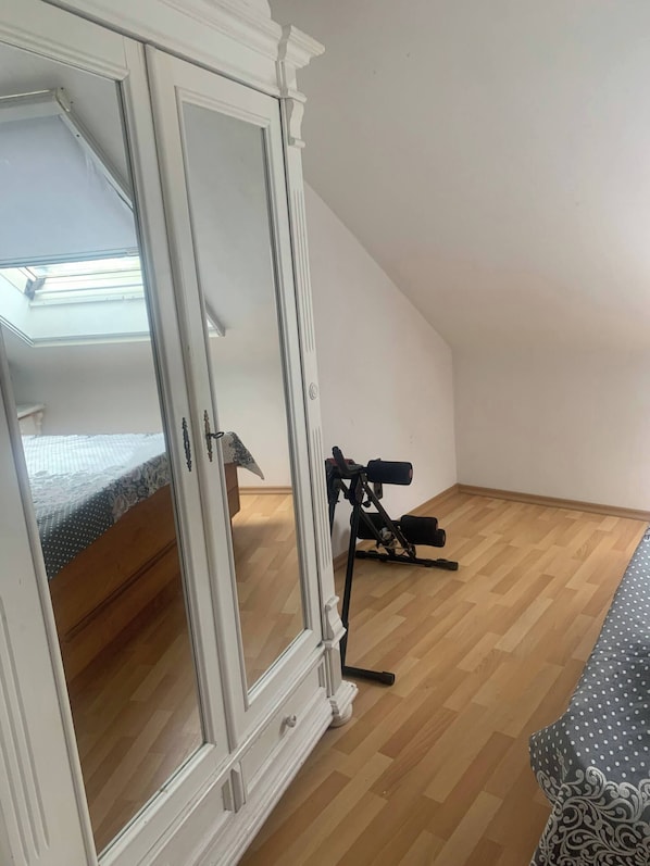 A room with a wooden floor, a bed with a patterned bedspread, a white wardrobe, and a tripod with a camera. - Pure Relaxation Quiet and Cozy (Weyhausen)