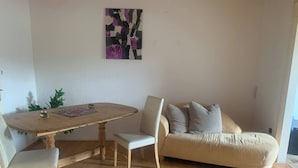 Un comedor con una mesa y sillas de madera, un sofá y un cuadro abstracto colgado en la pared.
