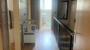 Un pasillo con suelo de madera, un banco blanco, una barandilla negra y una puerta que da a un baño.