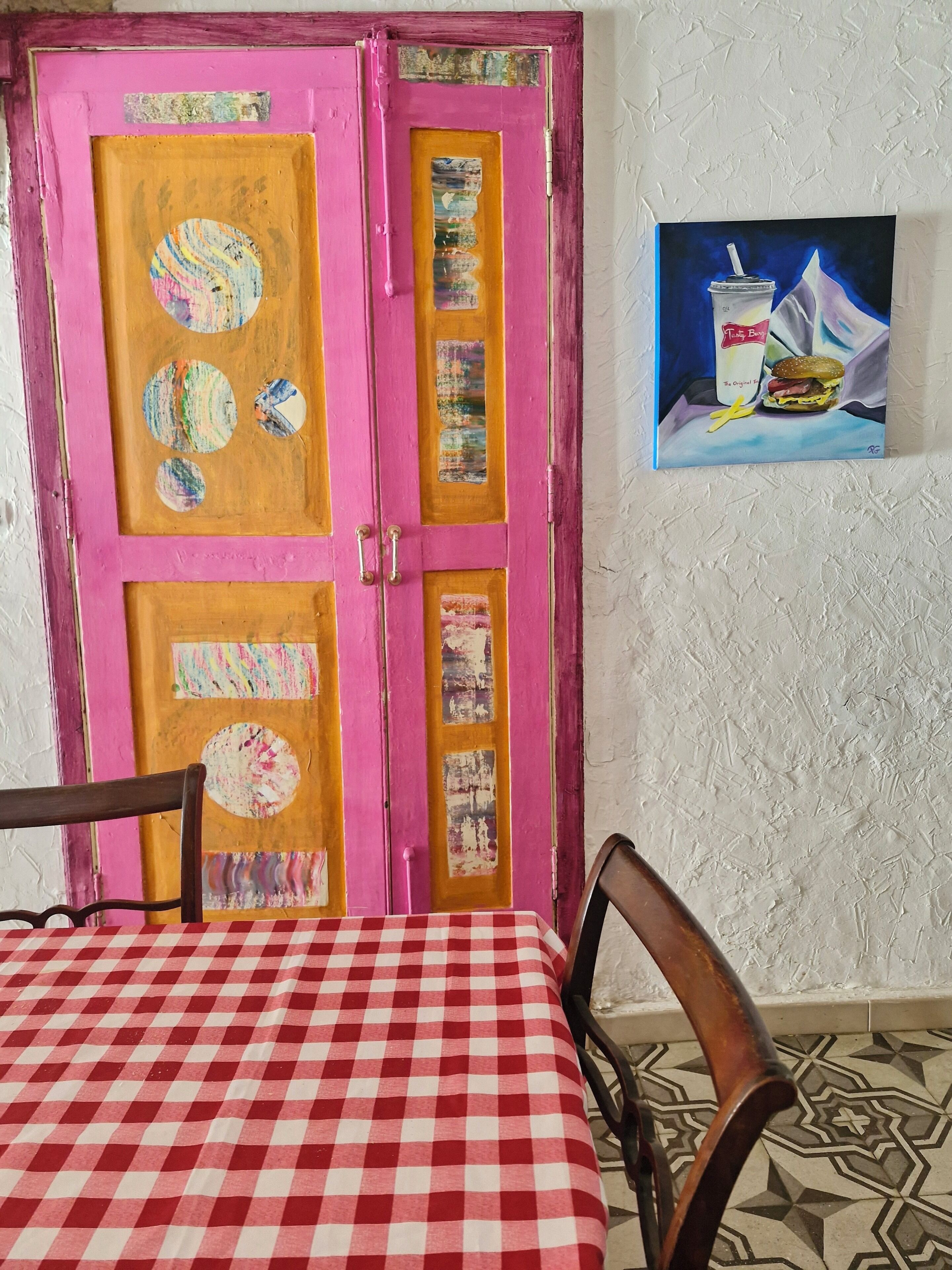A room with a pink door, a checkered table, and a painting of a drink and burger.