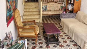 Ein gemütliches Wohnzimmer mit einem gemusterten Boden, einer Couch, einem Sessel, einem kleinen Tisch und einer Treppe, die in einen anderen Raum führt.