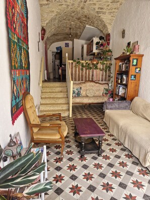 Ein gemütliches Wohnzimmer mit einem gemusterten Boden, einer Couch, einem Sessel, einem kleinen Tisch und einer Treppe, die in einen anderen Raum führt.